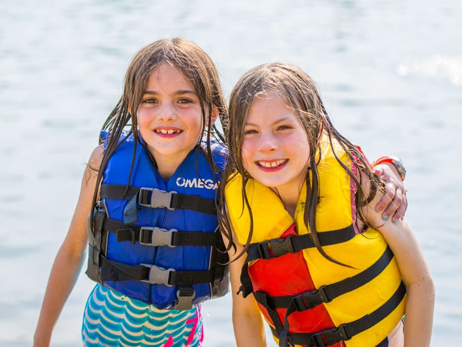 Two young girls wearing life jackets by lake