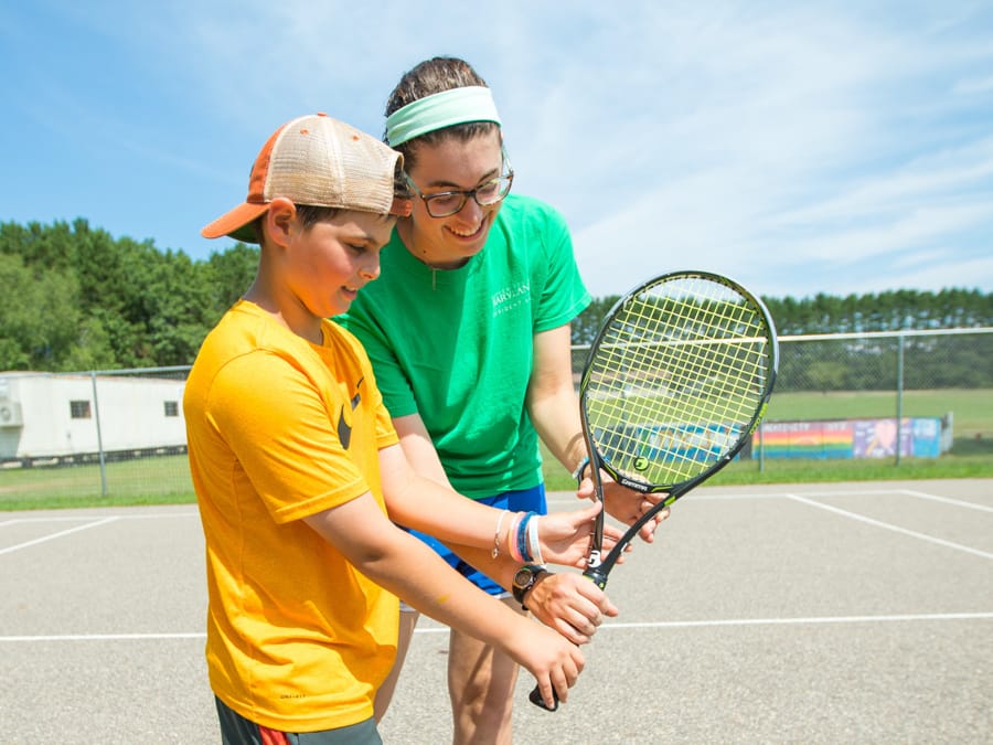 Tennis instructor teaching male camper how to hold racket